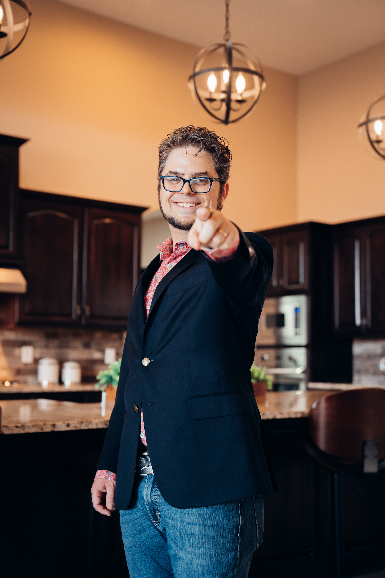  Picture of Avram Gonzales, Chief Strategist and SEO consultant at Digital Harvest pointing at the viewer. He is smiling, wearing a red paisley button up shirt with a dark blue sport jacket and glasses.