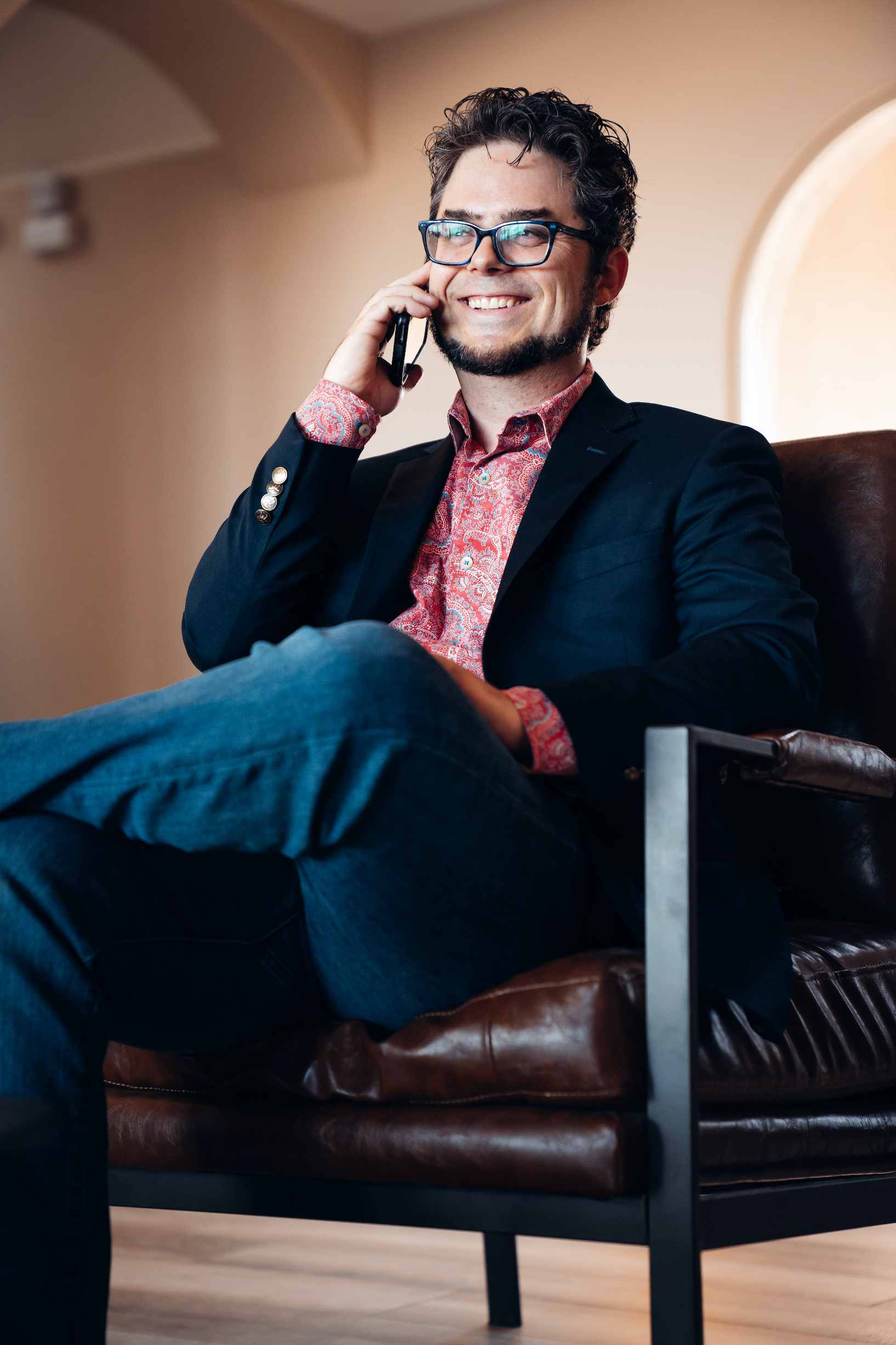 Picture of search engine optimization expert talking on the phone with a client in Albuquerque, NM. He is sitting with one leg crossed, smiling and gazing off camera.